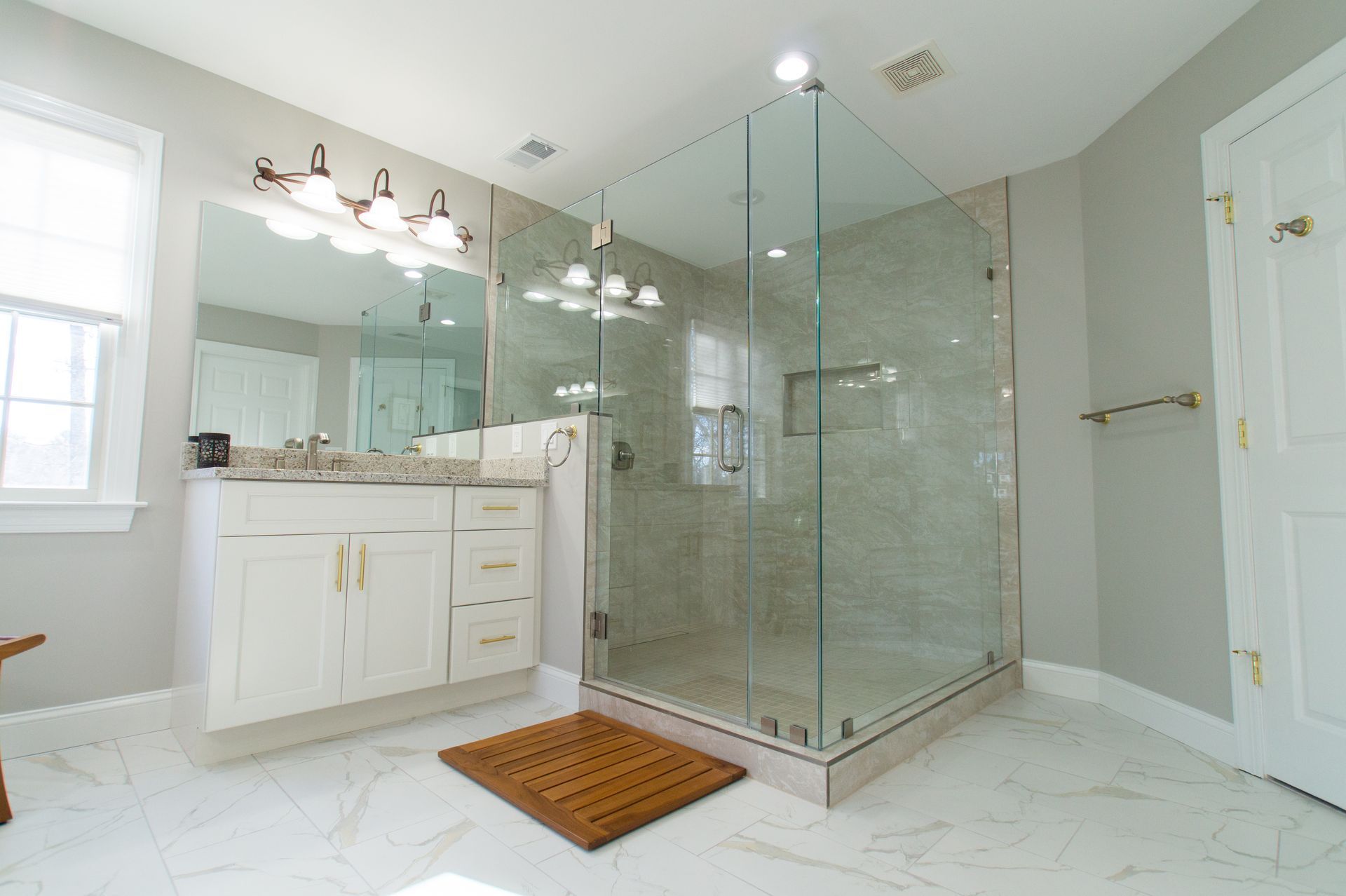 Bright bathroom with a large glass shower, white vanity, marble floors, and light gray walls.