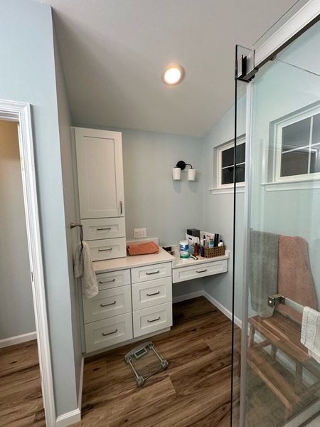 Bathroom with white cabinets, vanity, and shower. Light blue walls and wood-look flooring.