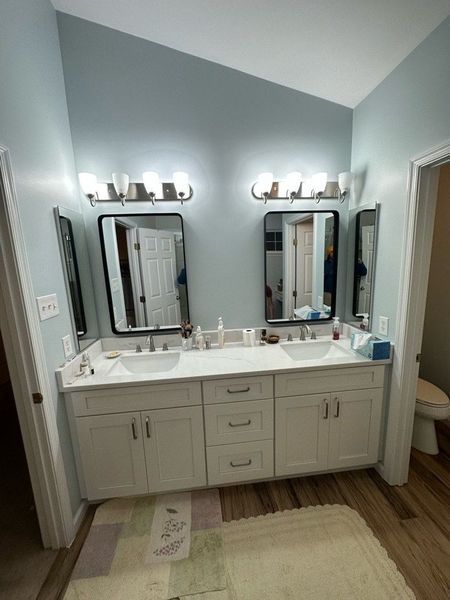 Bathroom with double vanity, two mirrors, and overhead lighting. Light blue walls, white cabinets, and wood flooring.