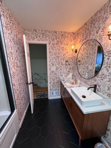 Bathroom with pink floral wallpaper, black hexagon tile floor, and a wooden vanity.
