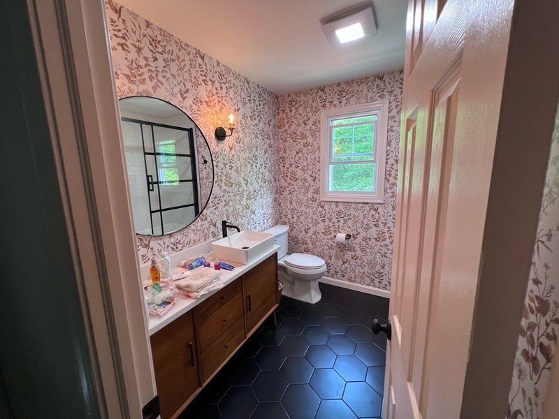 Bathroom with floral wallpaper, black hexagon floor tiles, and wood vanity.