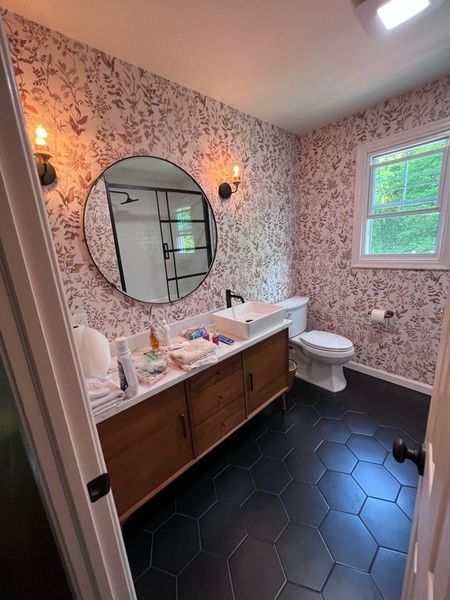 Bathroom with floral wallpaper, black hexagon tile floor, and a wooden vanity.