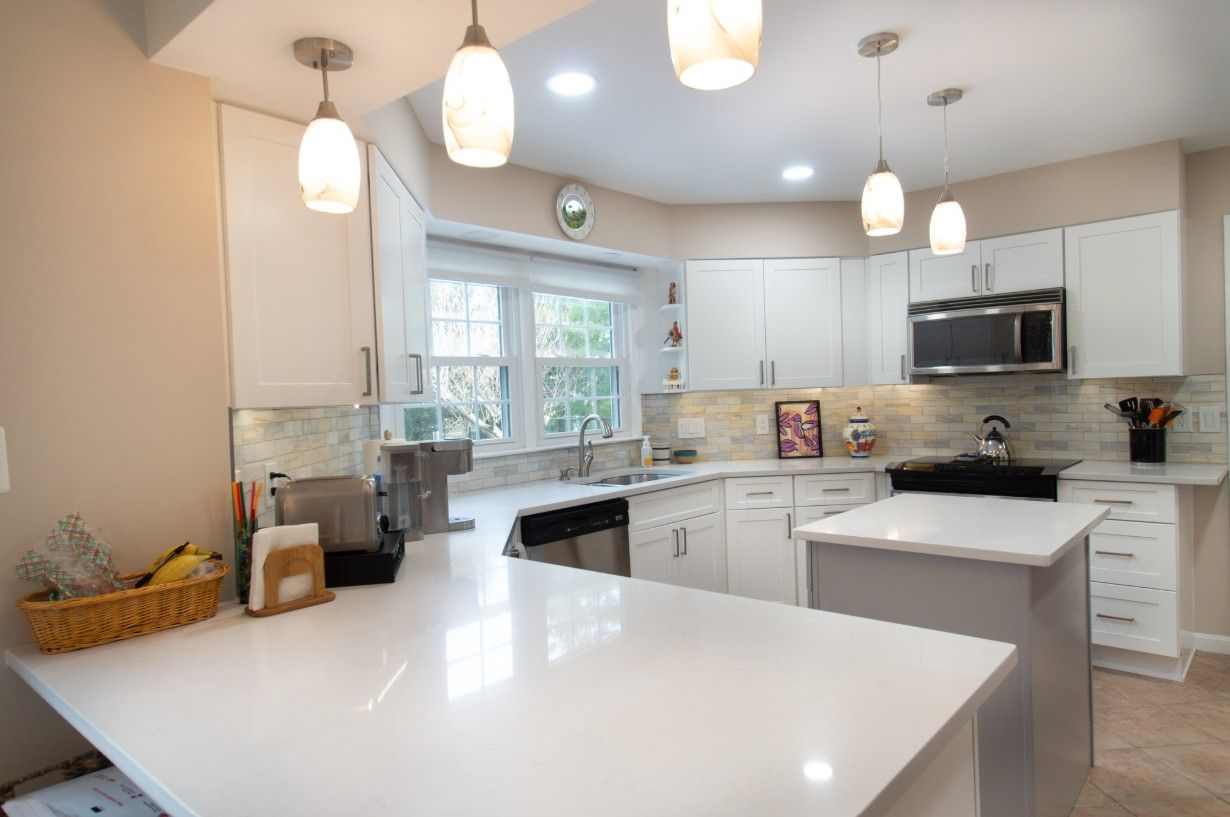Modern white kitchen with island, countertops, and pendant lights.