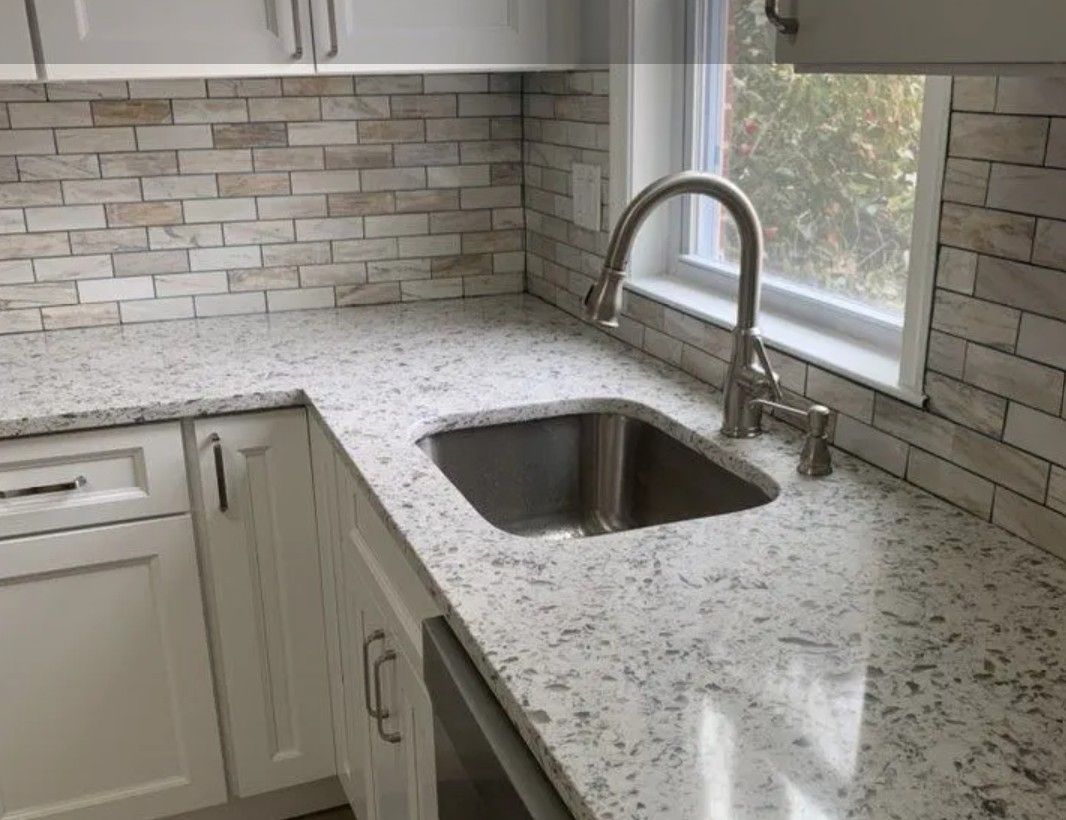 Kitchen sink with granite countertop and brick backsplash.