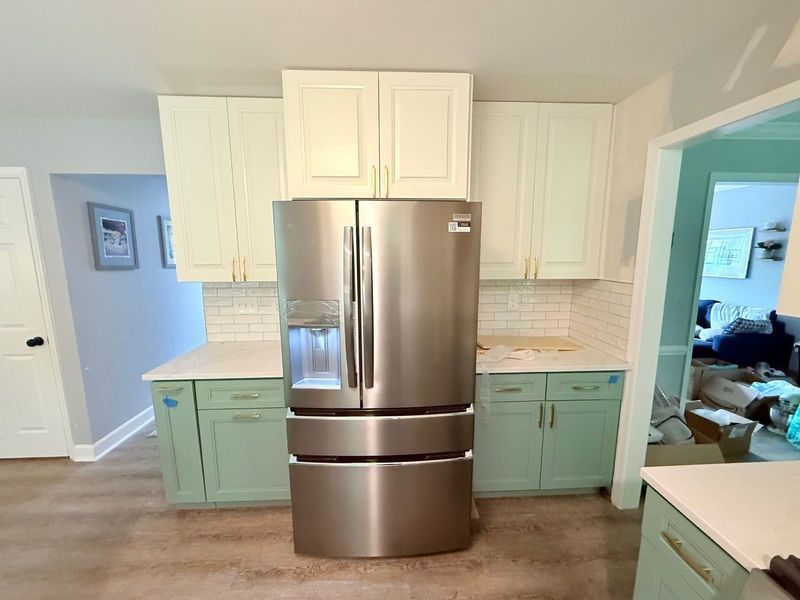 A newly renovated kitchen with stainless steel refrigerator, white and green cabinets, and light countertops.