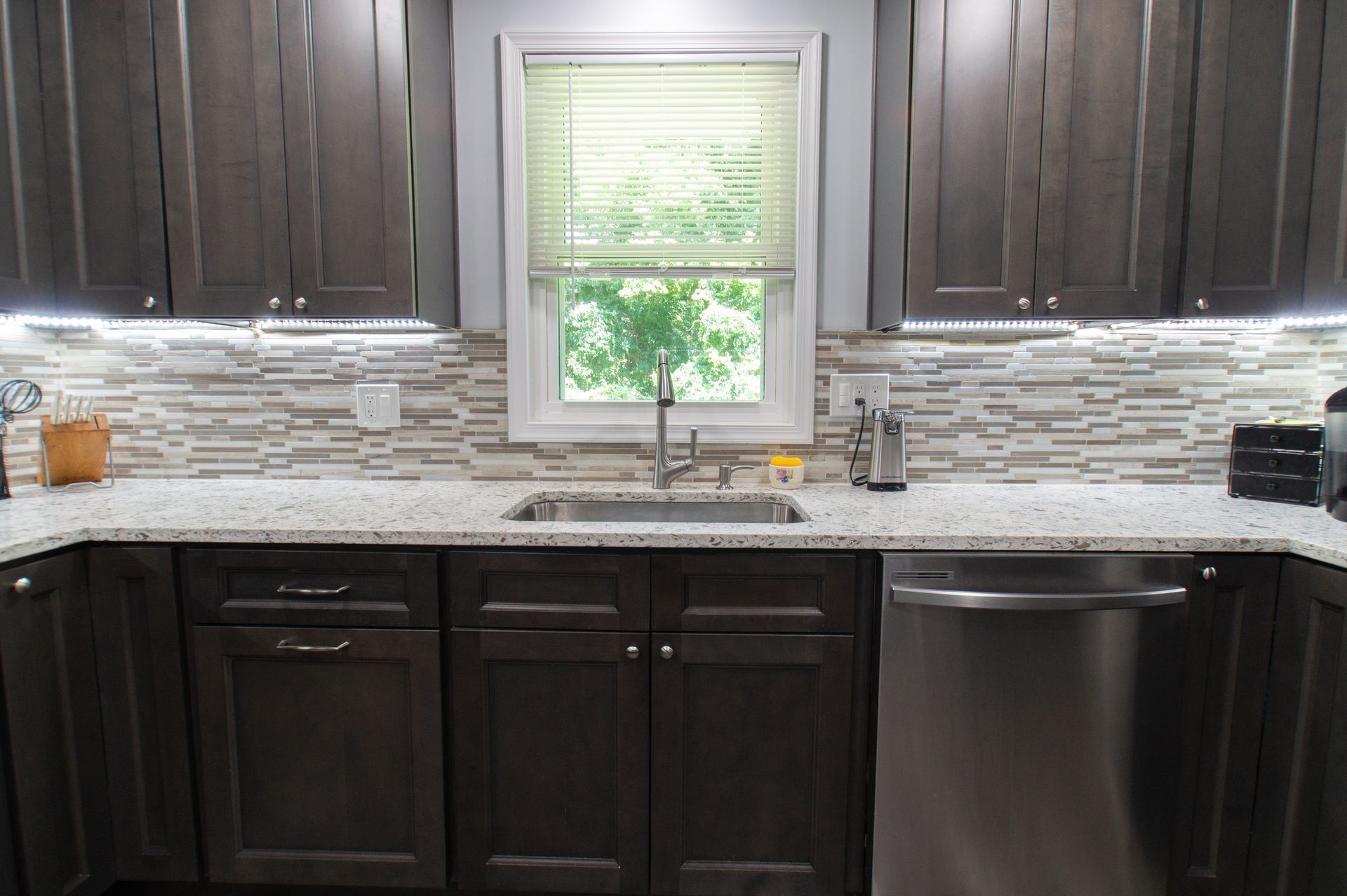 Kitchen with dark brown cabinets, a stainless steel sink, and a window with a green view.