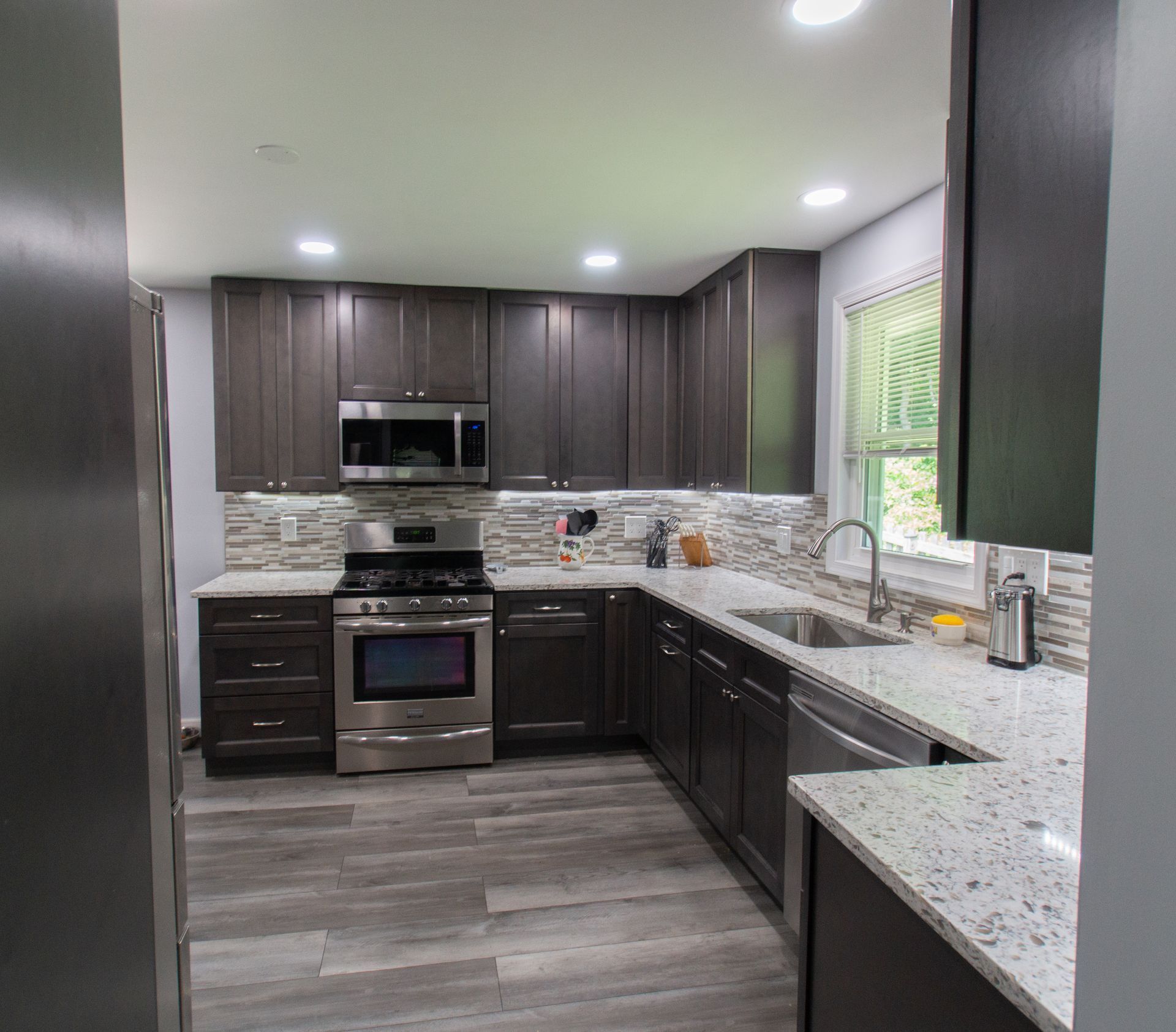 Dark brown kitchen with stainless steel appliances, speckled countertops, and wood-look flooring.