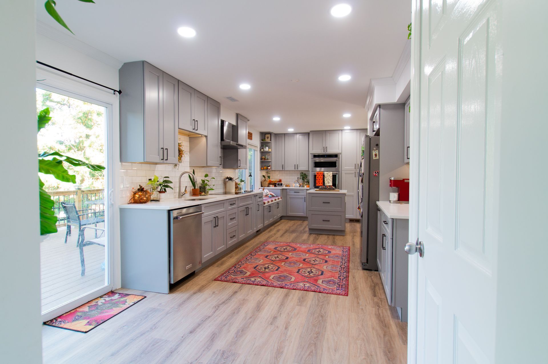 Gray kitchen with light wood floors, cabinets, and a colorful rug, opening onto a patio.