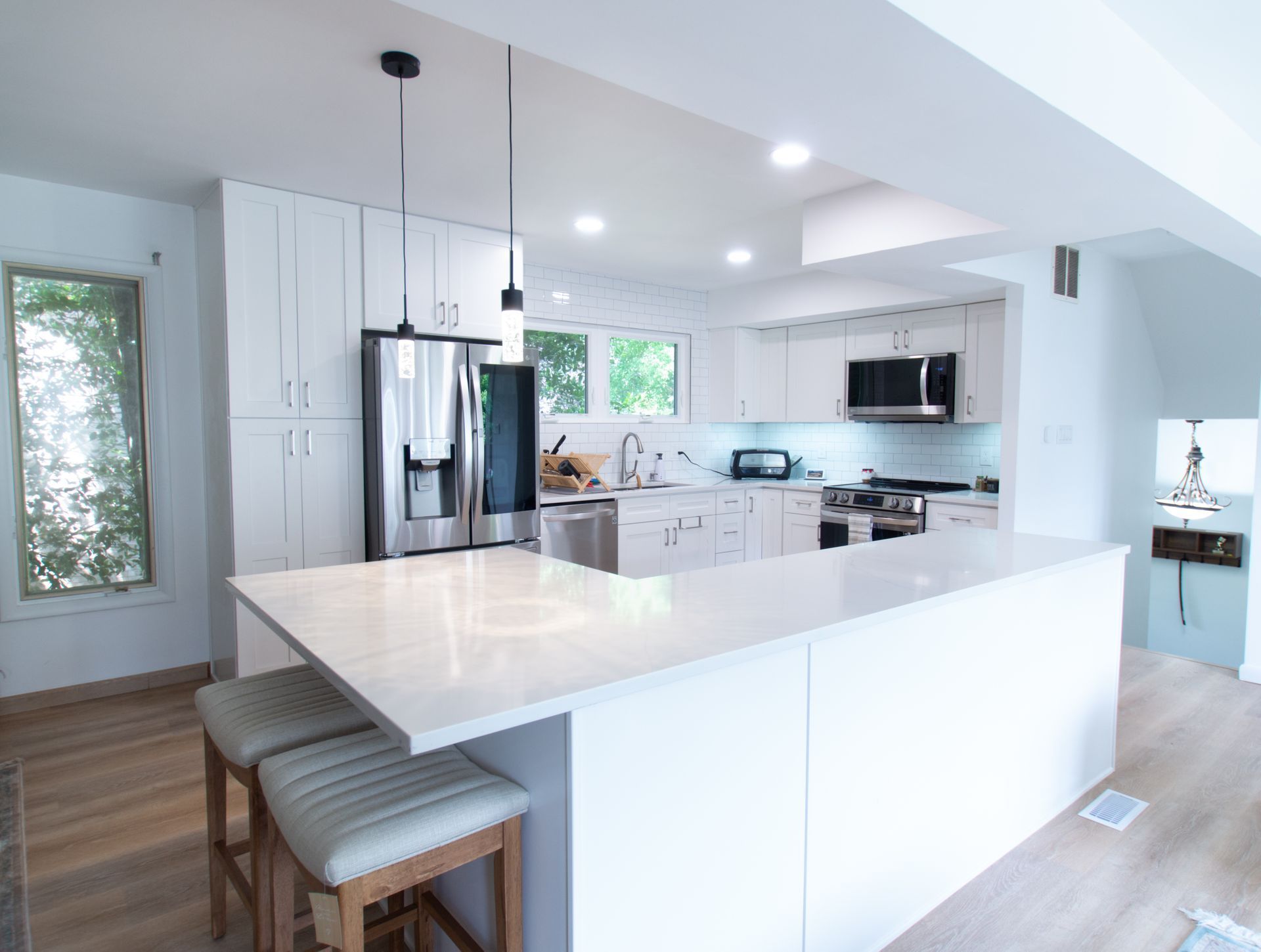 Modern white kitchen with island, stainless steel appliances, and two stools.