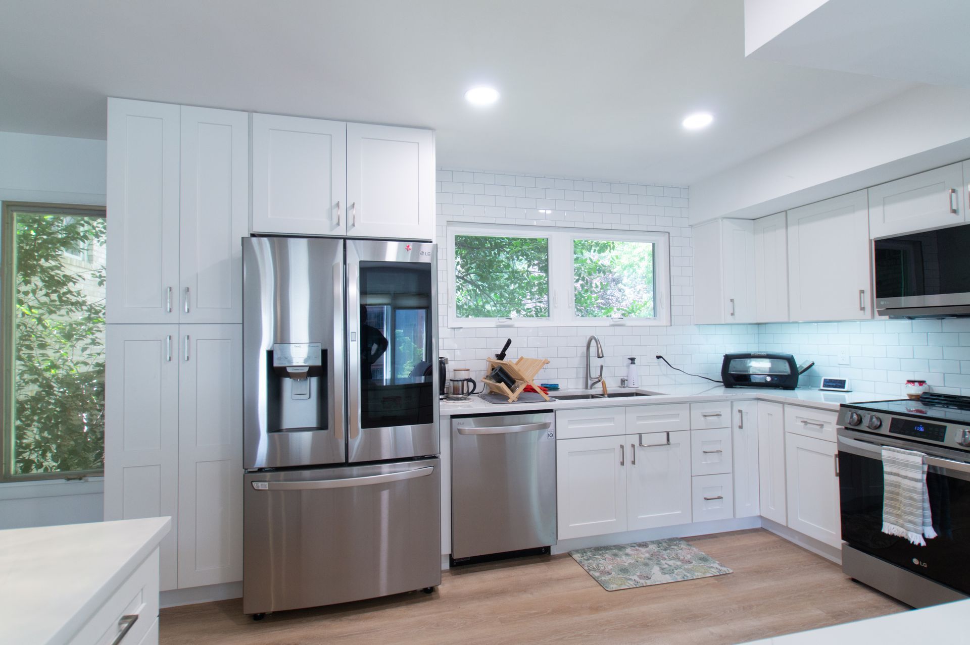 Bright white kitchen with stainless steel appliances, white cabinets, and a window overlooking greenery.