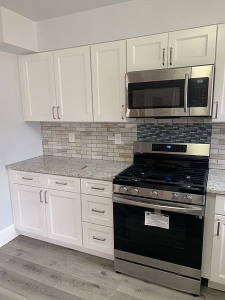 White kitchen cabinets with granite countertops and a stainless steel oven and microwave.