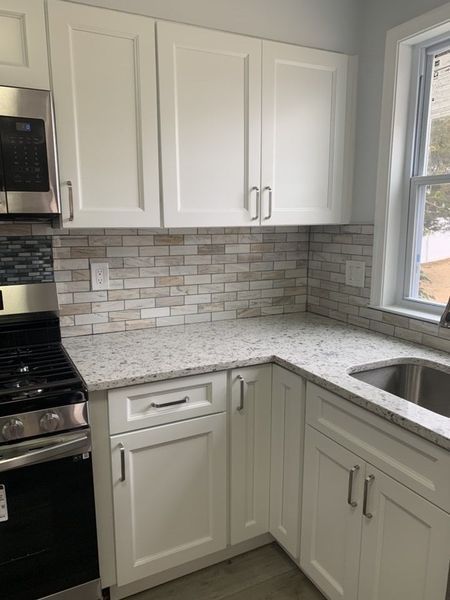White kitchen cabinets with granite countertops and brick-like tile backsplash next to a window.