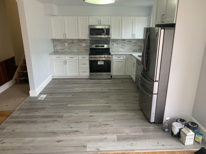 Modern kitchen with white cabinets, stainless steel appliances, grey flooring, and a stone backsplash.