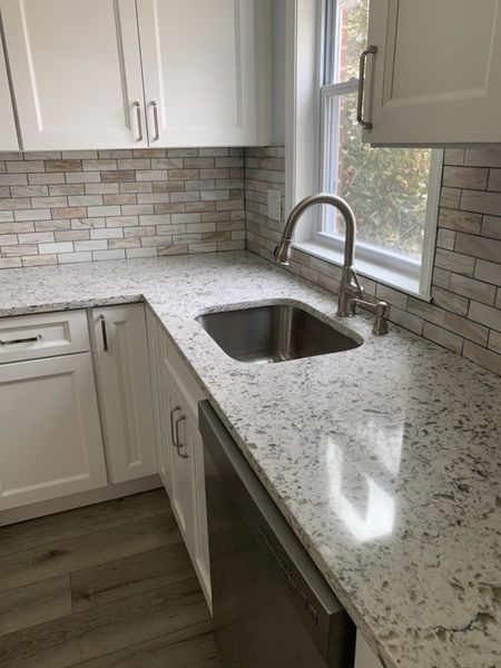 White kitchen with granite countertops, stainless steel sink, and light-colored brick backsplash.