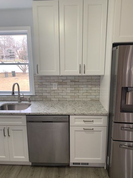 White kitchen cabinets with stainless steel appliances, granite countertops, and a tiled backsplash.