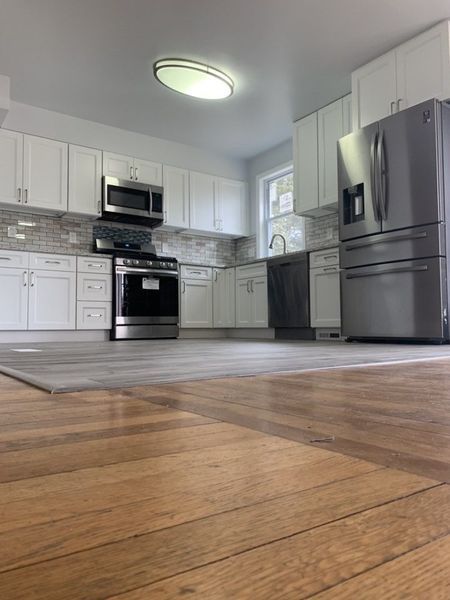 Modern kitchen with white cabinets, stainless steel appliances, and hardwood floors.