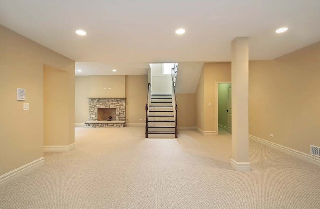 Beige basement room with fireplace, stairs, and door. Carpeted floor, beige walls.