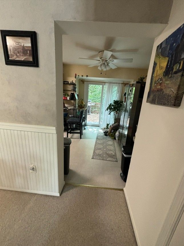 A hallway leading through an arched doorway into a living area with a ceiling fan, a glass sliding door, and carpet.