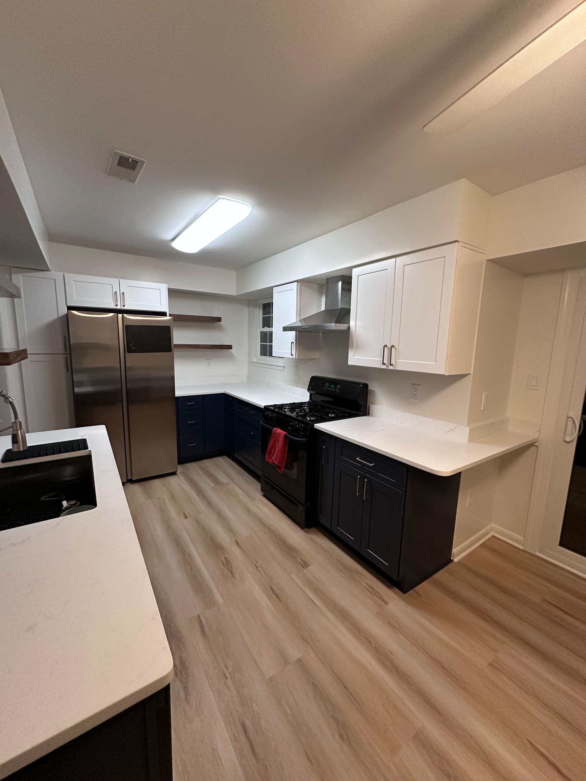 Modern kitchen featuring dark blue lower cabinets, white upper cabinets, stainless appliances, and light wood flooring.