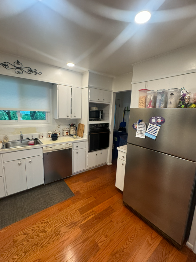 A kitchen featuring white cabinets, stainless steel appliances, a gray floor mat, and wood floors.