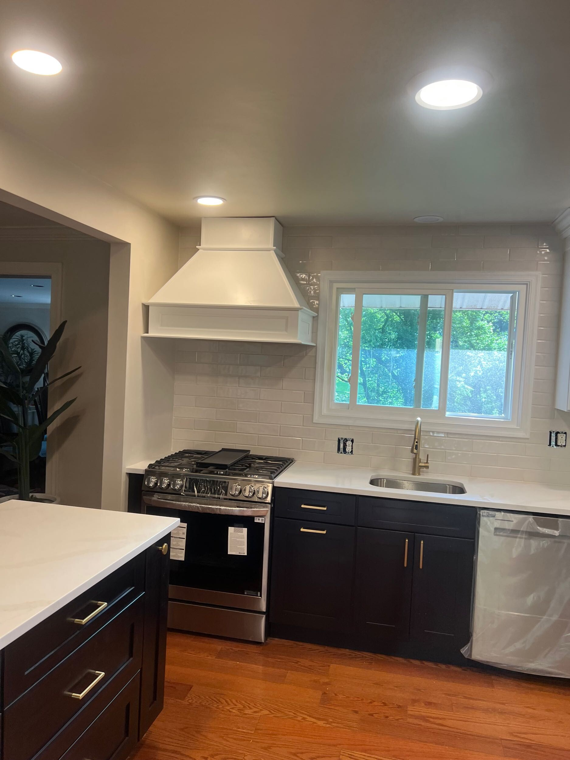A modern kitchen with dark blue cabinets, white countertops, a gas range with a white vent hood, and light wood floors.