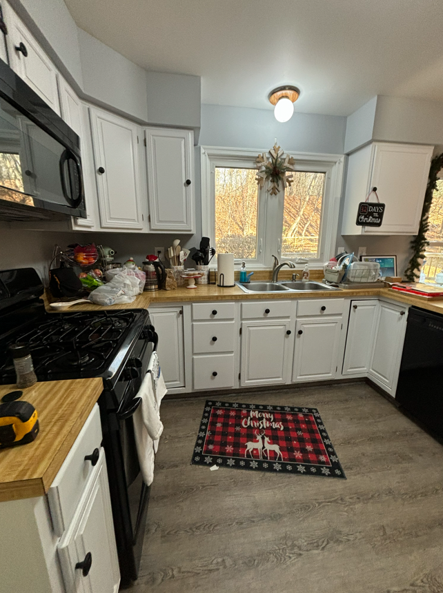 A kitchen with white cabinets, wood-look countertops, black appliances, and a holiday-themed rug on the floor.