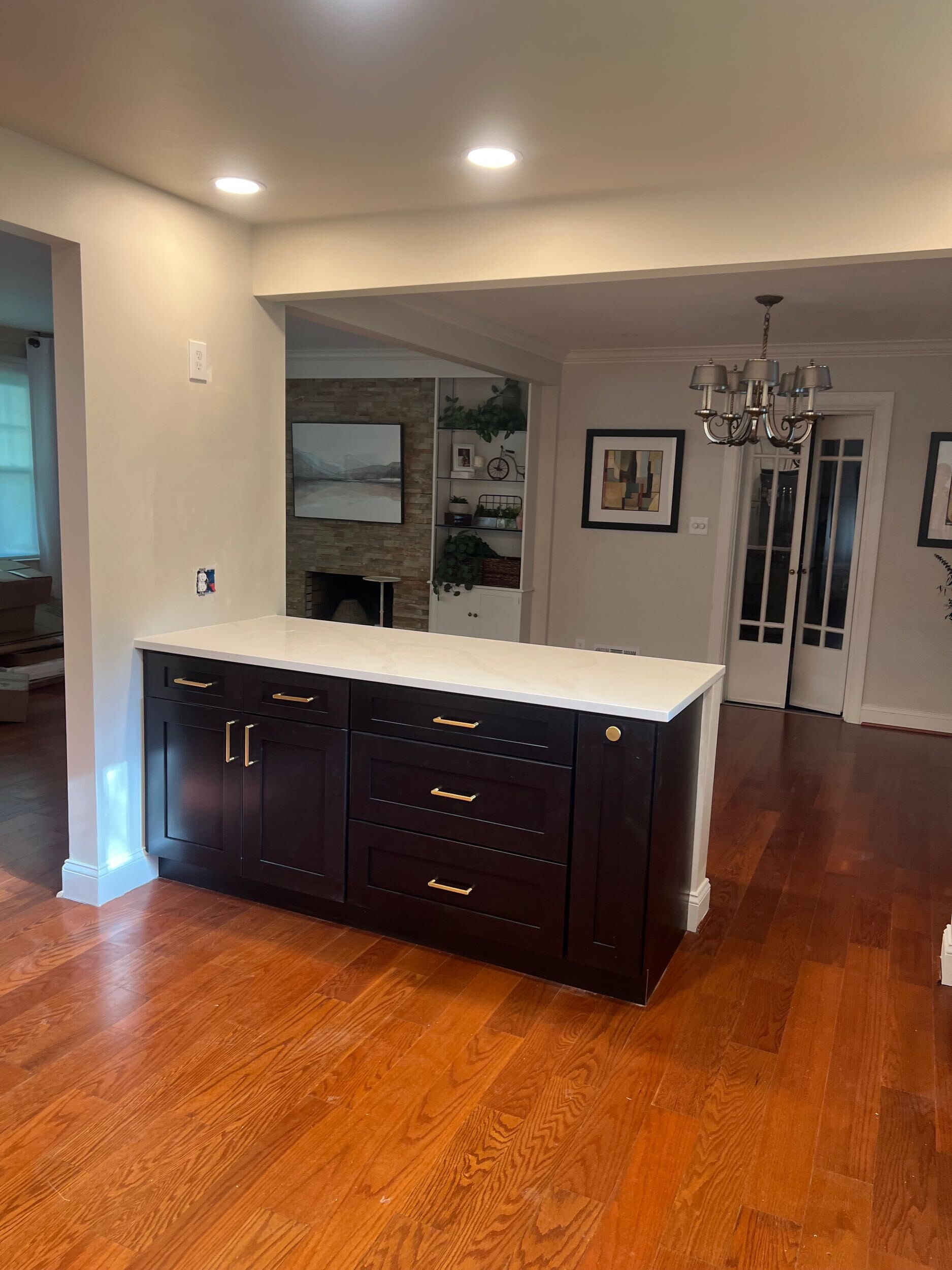 A kitchen island with dark brown cabinets and a white countertop stands on a hardwood floor in an open-plan home.