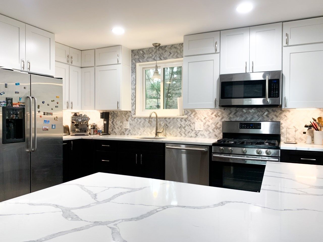 Modern kitchen with white upper cabinets, black lower cabinets, stainless steel appliances, and a marble countertop island.