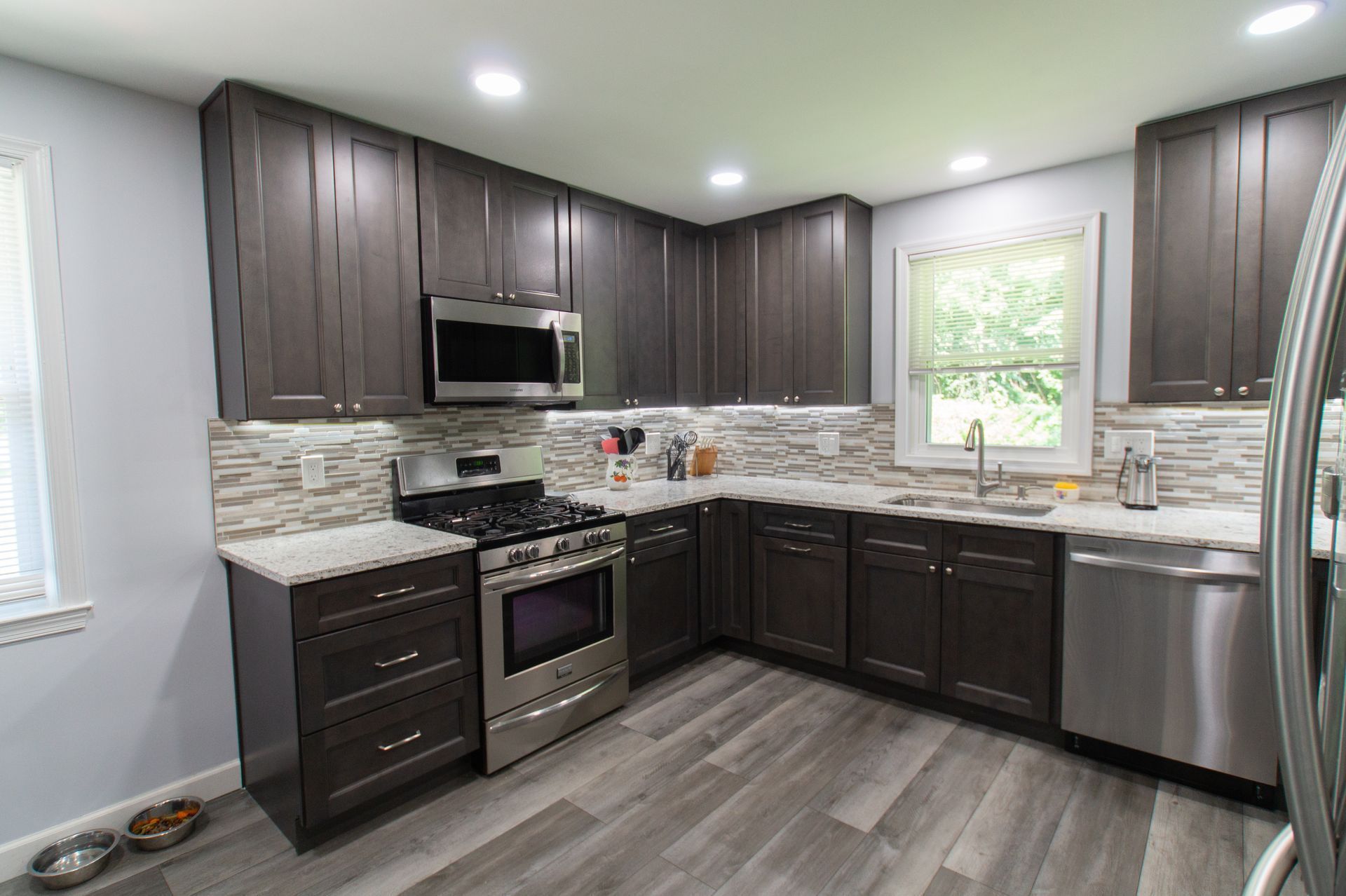 Dark gray kitchen with stainless steel appliances, white countertops, and gray wood-look flooring.