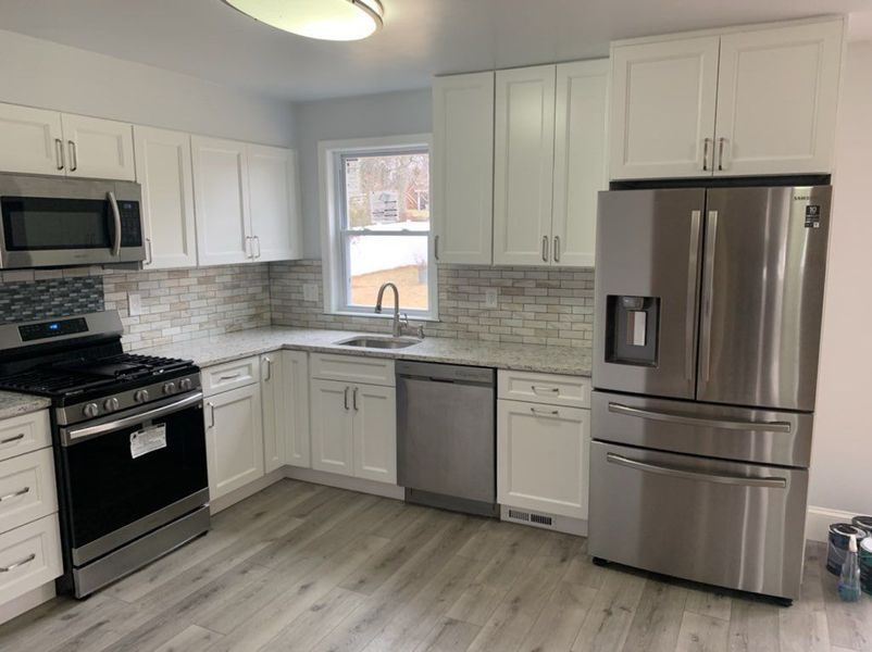White kitchen with stainless steel appliances, light gray flooring, and a window.
