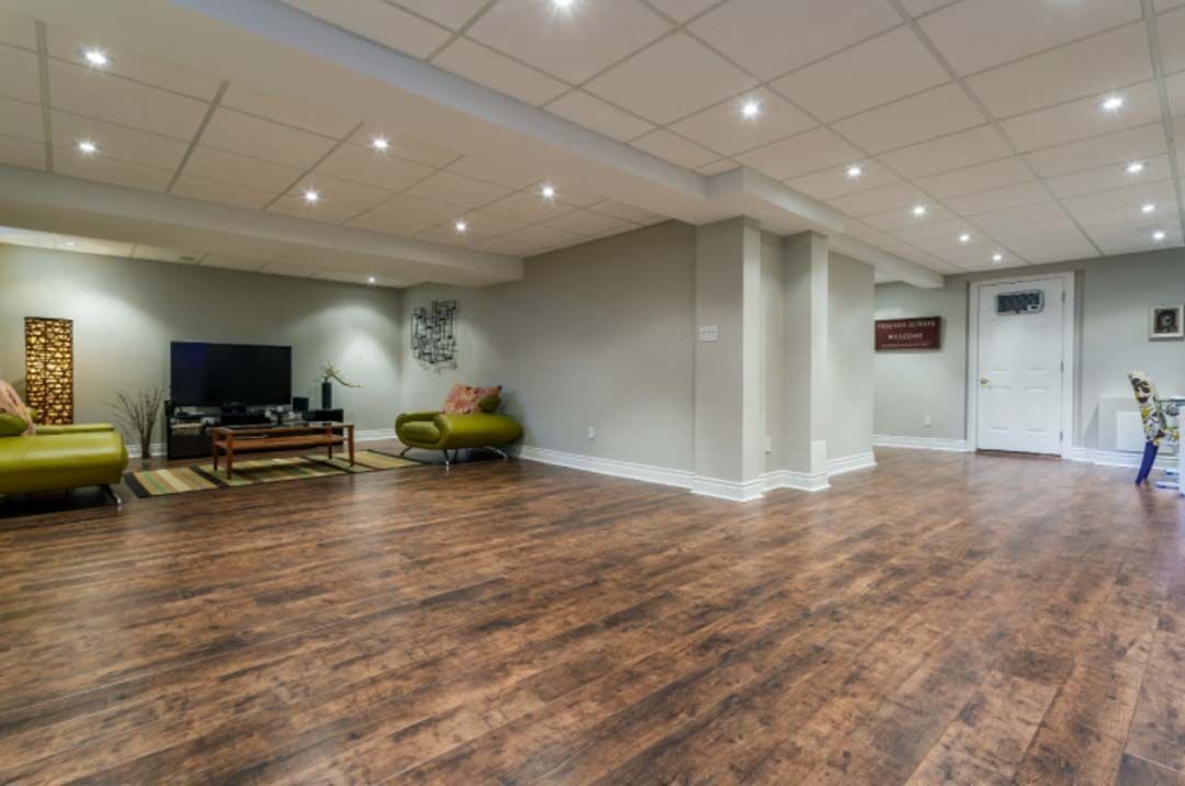 Large, empty basement living area with wood flooring, light gray walls, and recessed lighting.