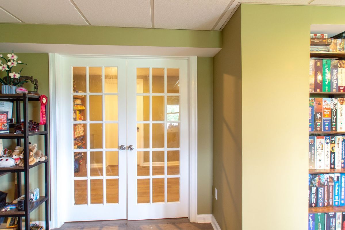 French doors in white frame, leading to another room. Shelving with books on right, light green and brown walls.