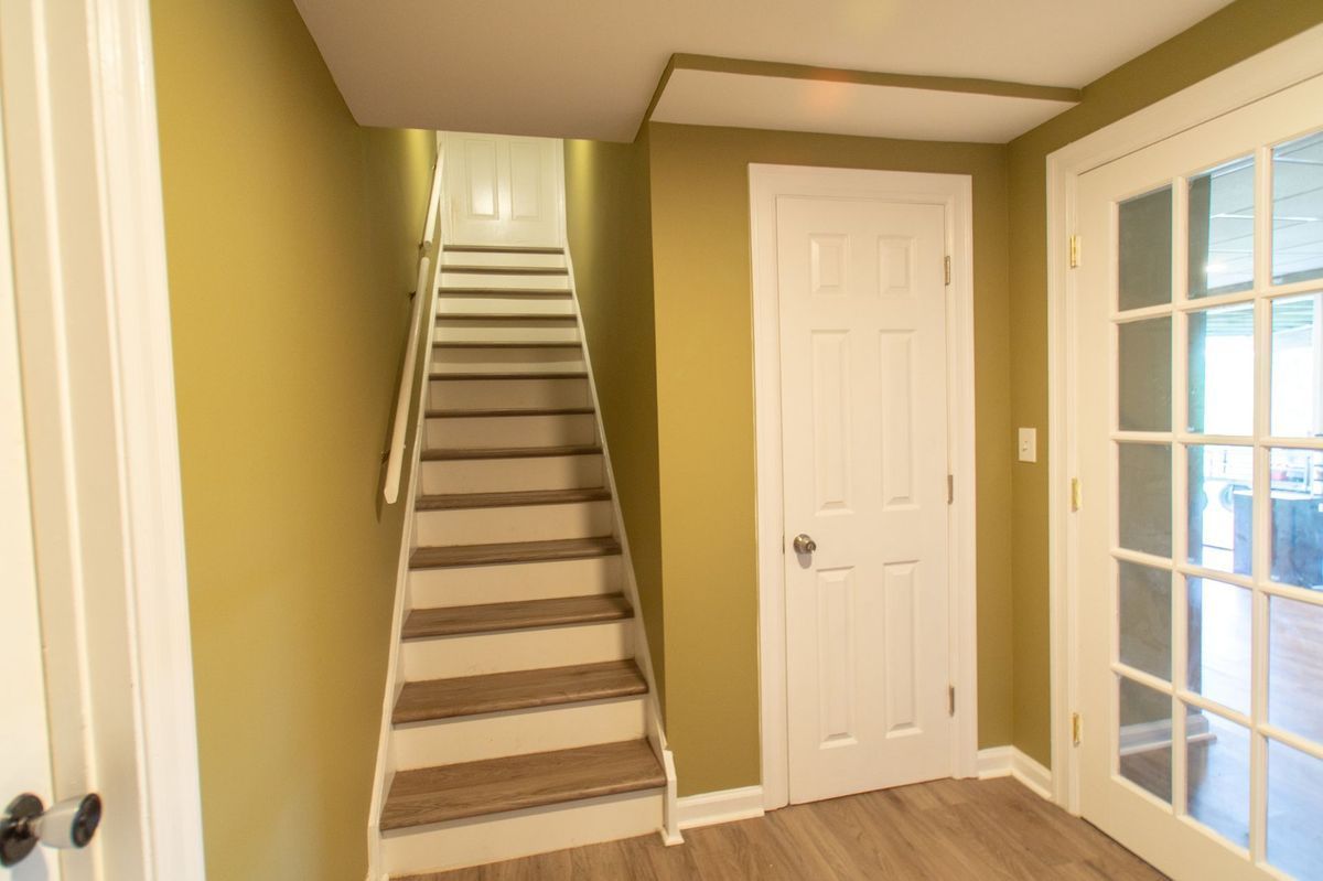 Staircase leading up, white door, and glass French doors in a room with yellow walls and wood-look flooring.