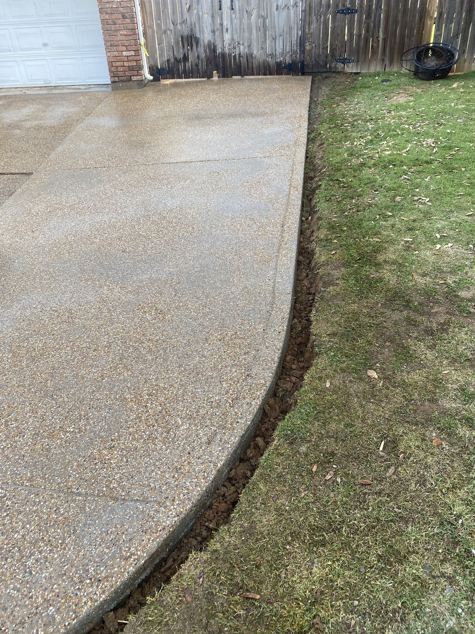Driveway edge alongside grass, with a dirt trench separating the two.