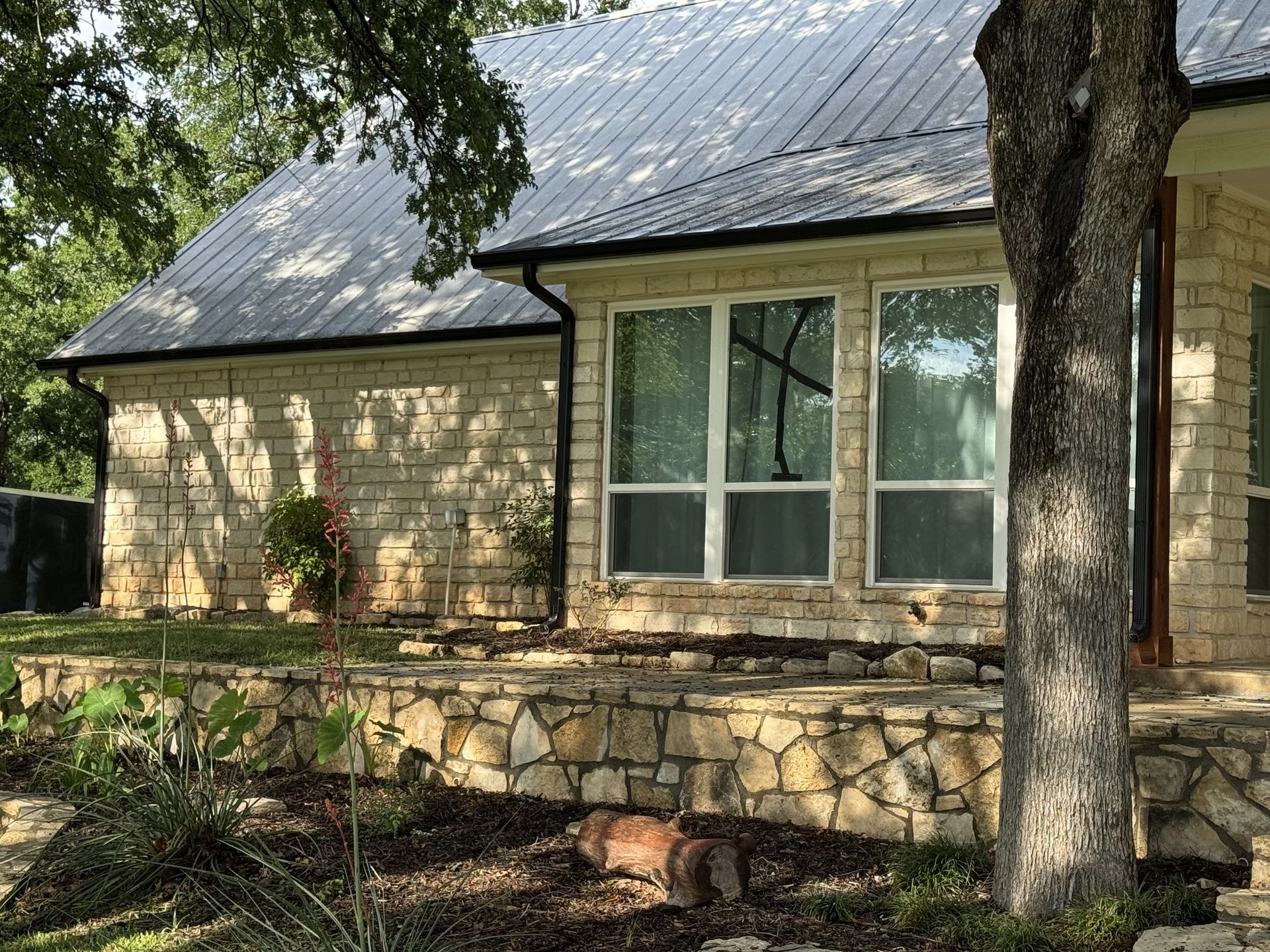 Stone house with metal roof, large windows, and a tree in front.