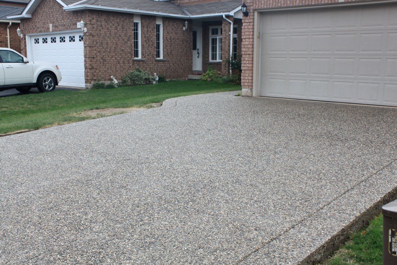 Exposed aggregate concrete driveway leading to a brick house with a garage and a white car.