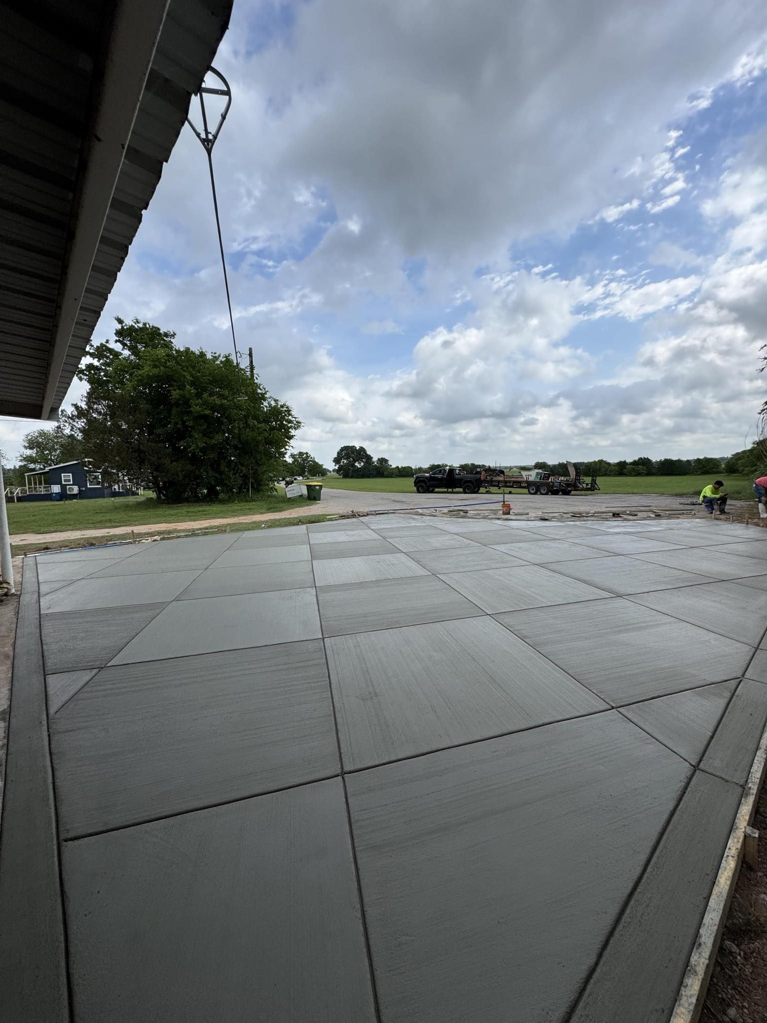 Newly poured concrete patio, divided into squares, under a cloudy sky.