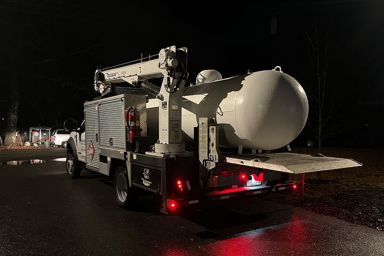 A tow truck with a large tank on the back is parked in a parking lot at night.