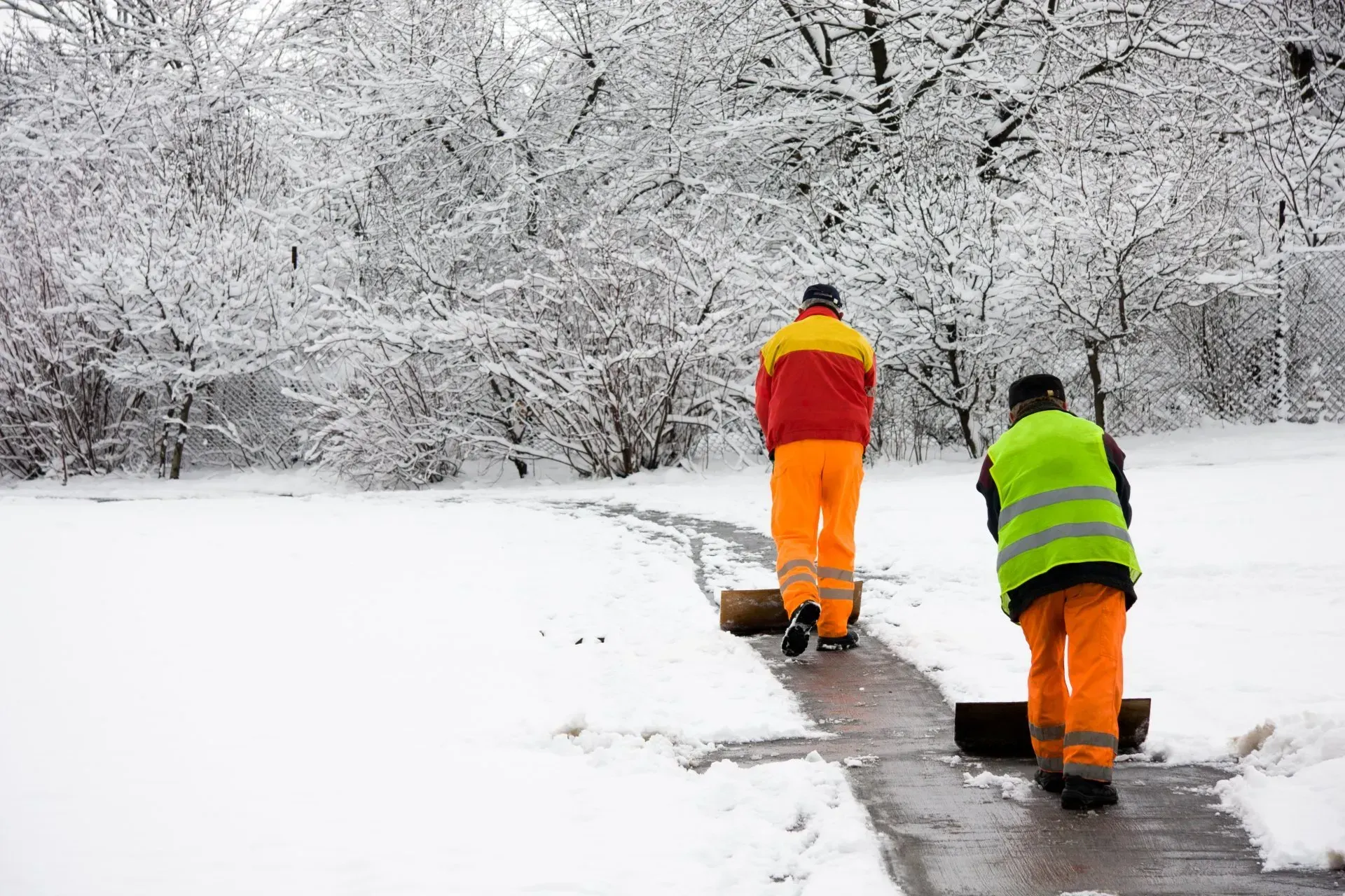 A silver truck is plowing snow in a driveway.