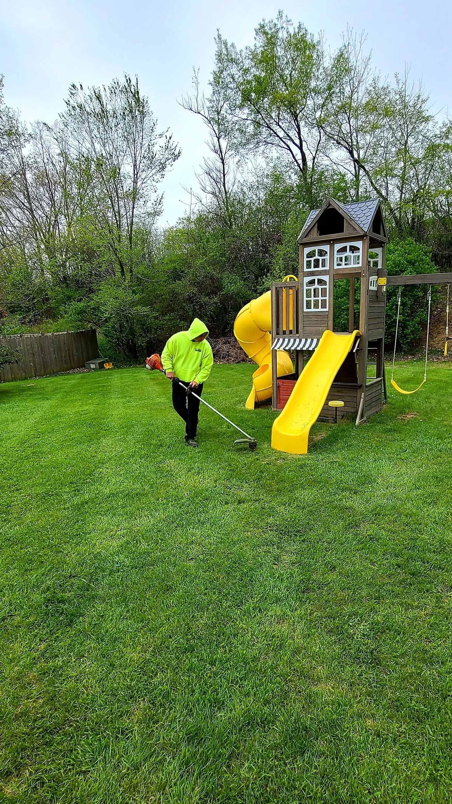 A man is mowing the grass in front of a playground.