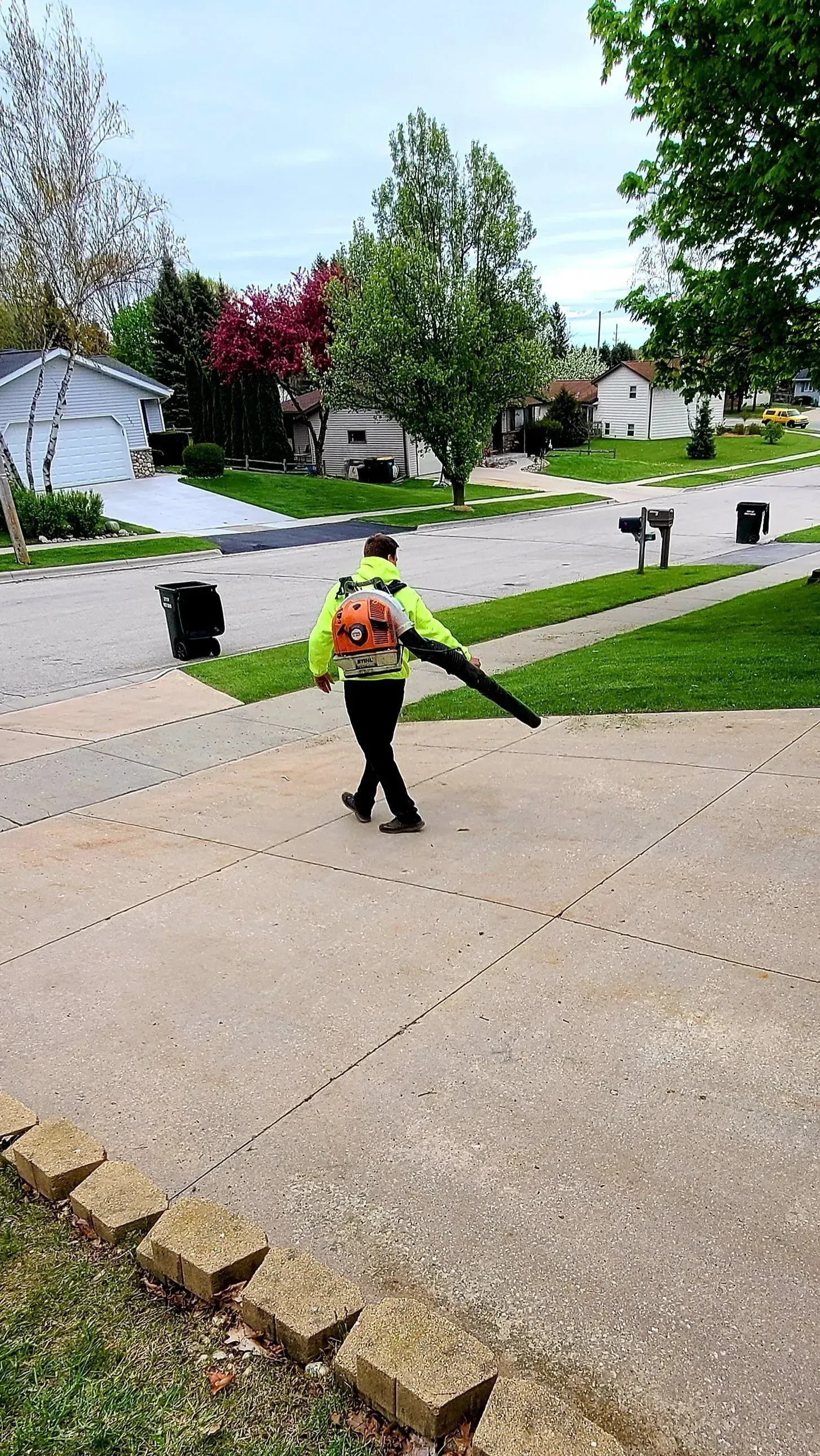 A man is walking down a sidewalk using a leaf blower.