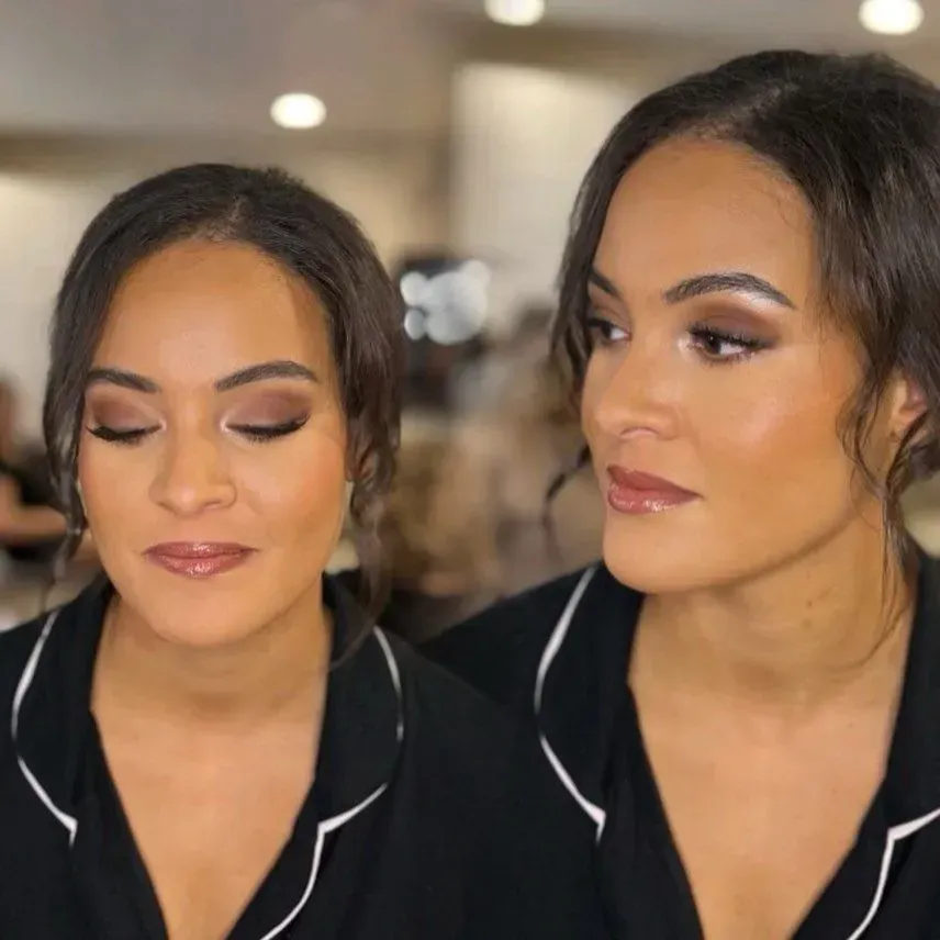 Two women with matching makeup and black tops posing indoors, one facing forward and one in profile