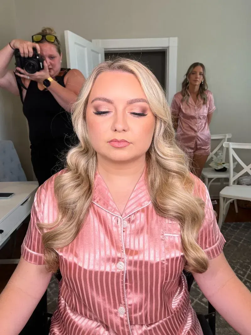 Woman in pink satin top getting her hair styled, with two people in the background