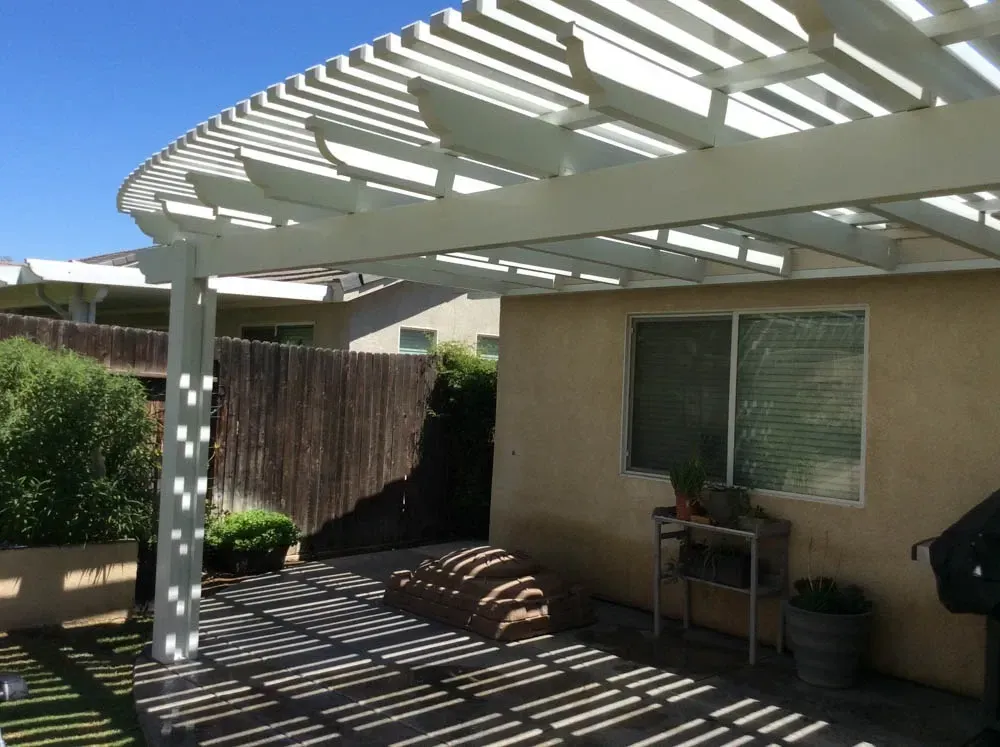 A white pergola is covering a patio in front of a house.