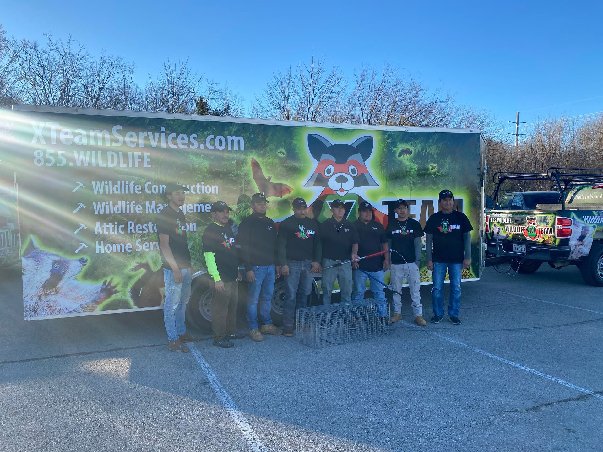 Group of people posing beside a truck with a large raccoon mural and banner in a parking lot.