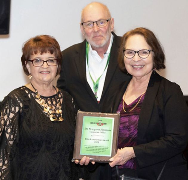 Three people posing with an award plaque, two women in front and a man behind them.