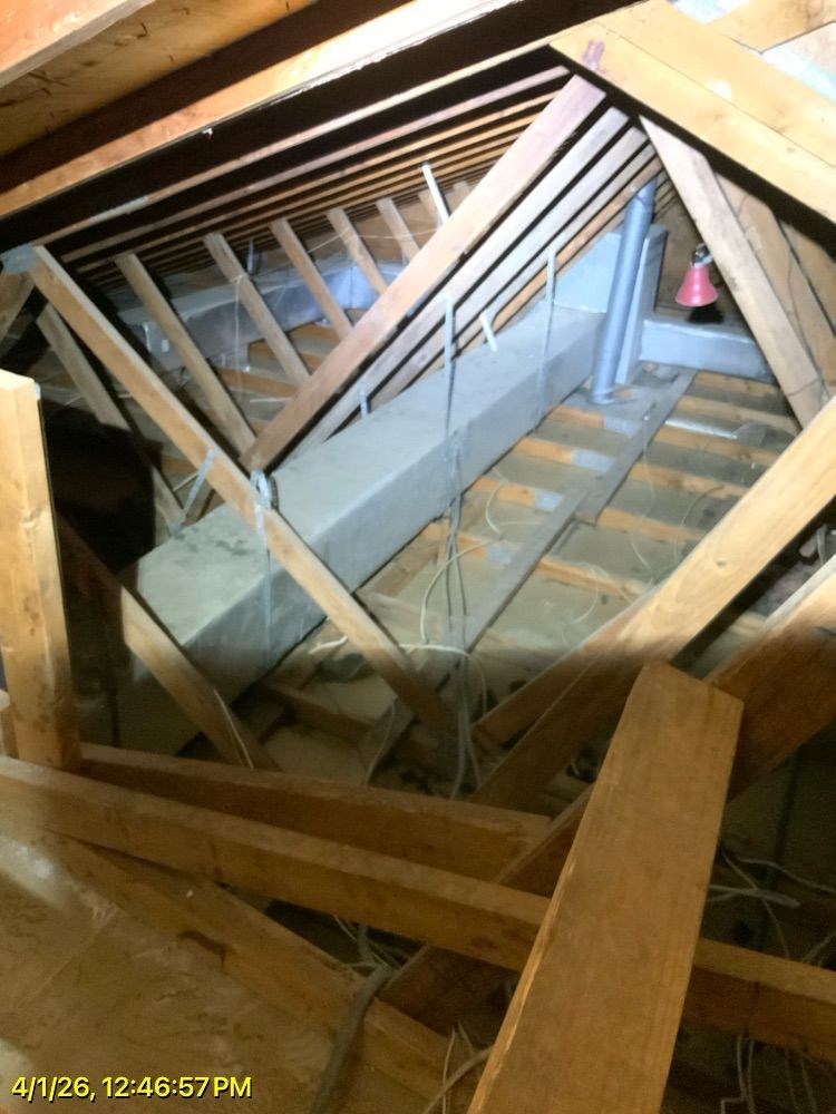 Collapsed attic roof framing with exposed wooden beams and a damaged skylight opening.