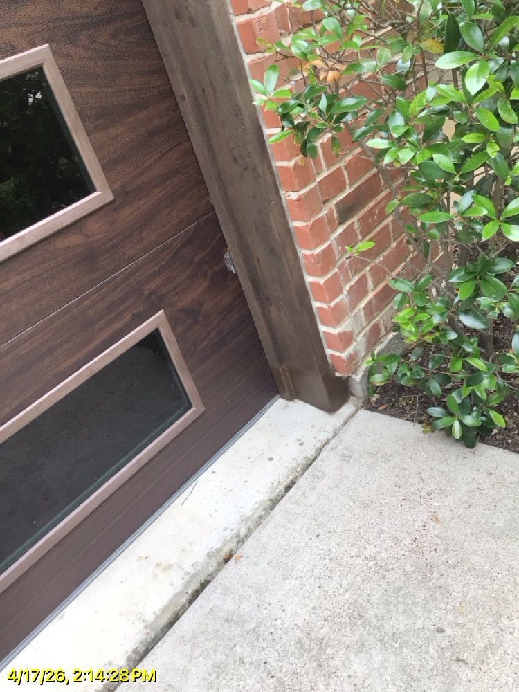 Close-up of a wooden door beside a brick wall, with concrete porch and leafy shrub.
