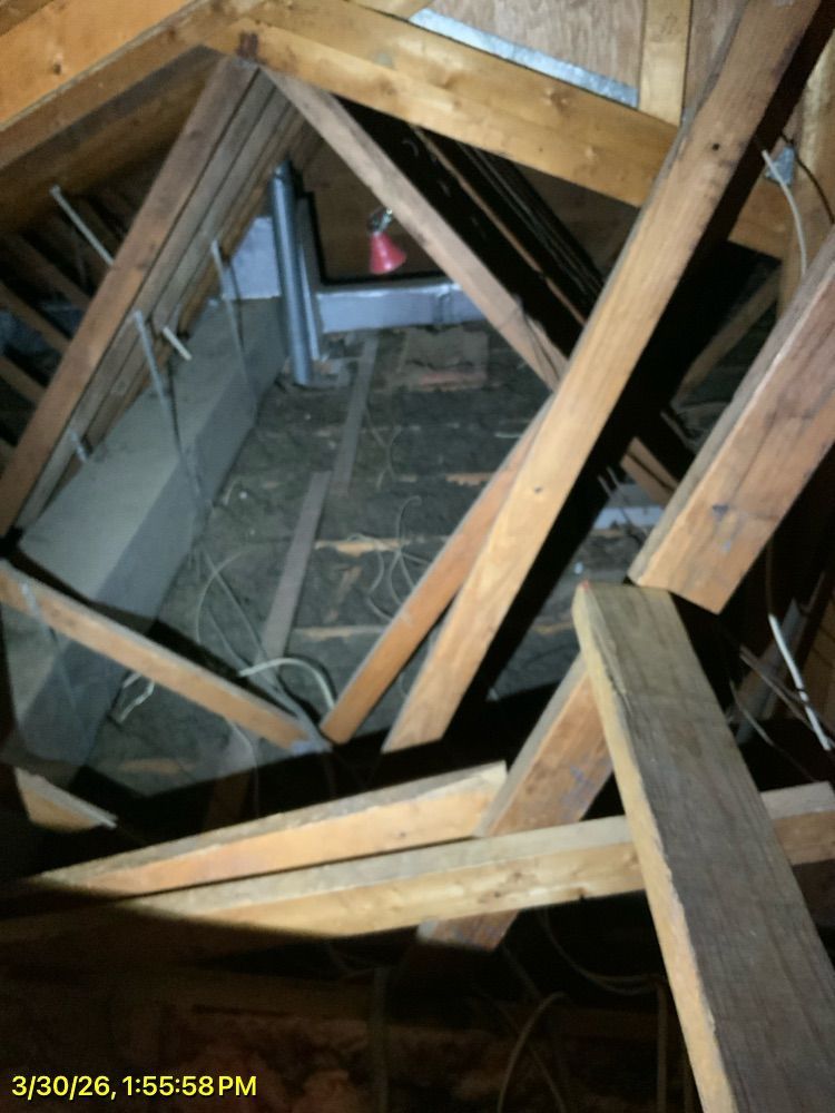 Damaged attic framing with exposed wood beams and a collapsed central opening leading downward.