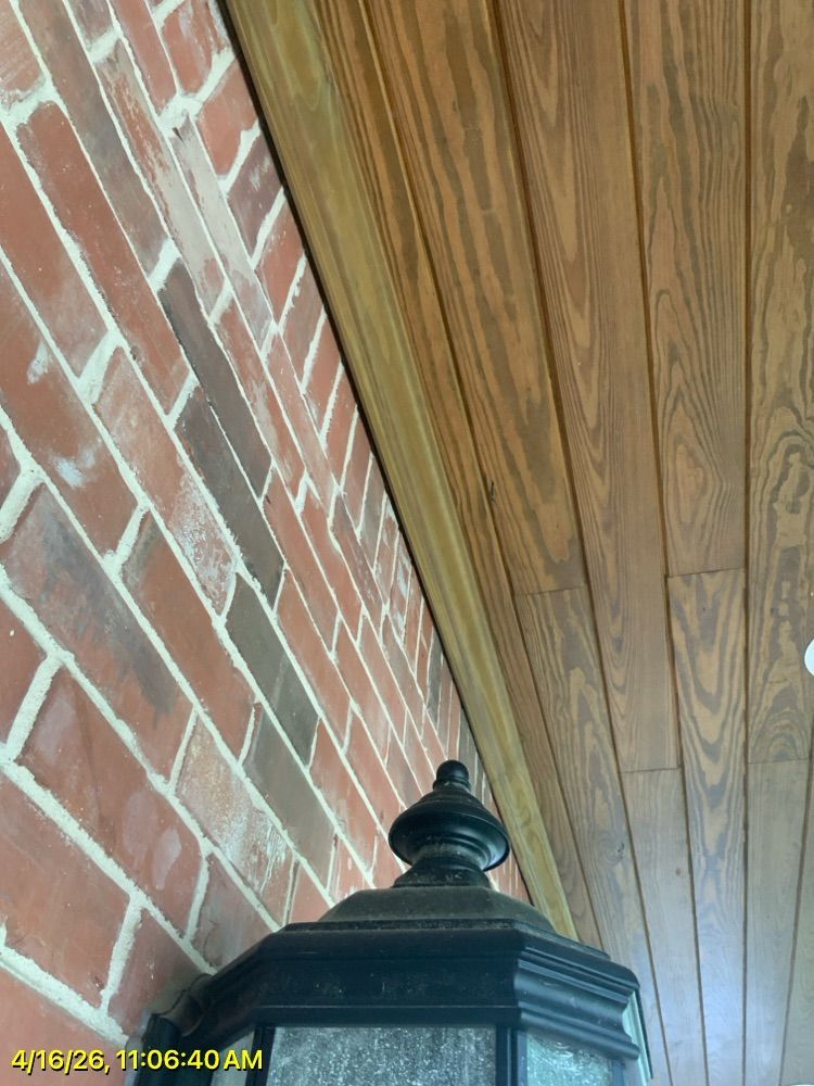 Brick wall and wood-paneled ceiling corner above a black lantern at the porch edge.